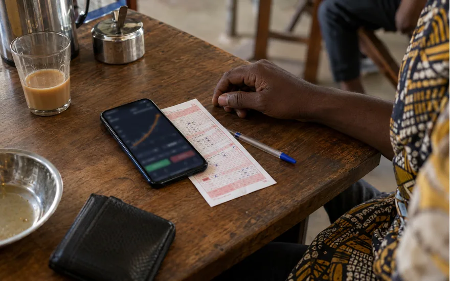overhead of smartphone with abstract crash game curve, adult dark-skinned hand resting beside betting coupon, local interior; understanding an Aviator round. Illustrative generated scene.
