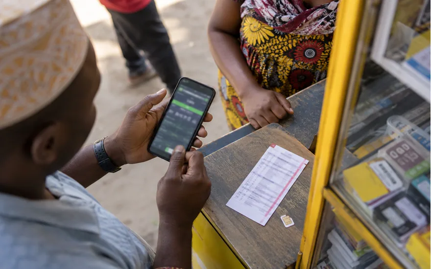 overhead of affordable phone with blurred sports betting registration and unbranded SIM card at local telecom kiosk, no personal data visible; opening a Tanzania account. Illustrative generated scene.