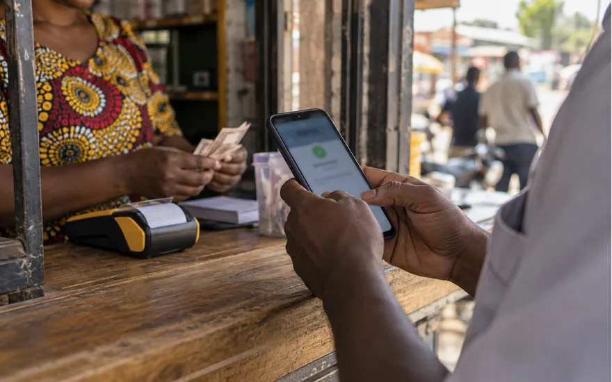 Mikono ya mtu mzima na simu yenye taarifa za malipo kwenye kibanda cha huduma za fedha Tanzania
