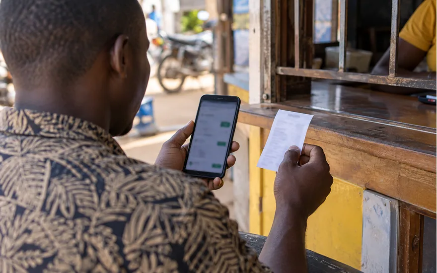 Mikono ya mtu mzima na simu inayoonyesha taarifa za mchezo au malipo; kufuatilia ombi la kutoa pesa. Picha ya kubuni, si tukio halisi.