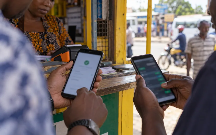 Adult hands comparing a generic mobile wallet confirmation and a blurred betting transaction screen on two phones at a Tanzanian payment agent kiosk; why betpawa is not working. Illustrative generated photograph, not an operator screenshot.